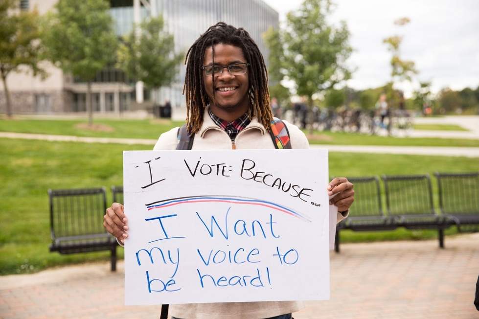 Student holding a sign reading "I vote because I want my voice to be heard"